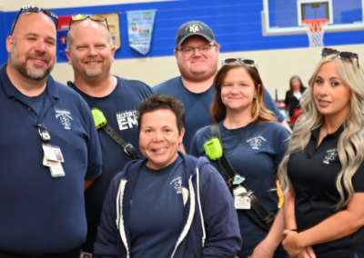 A team of men and women in navy t-shirts and black pants stand together.
