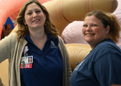 Two women in a navy t-shirt are smiling posing next to one another
