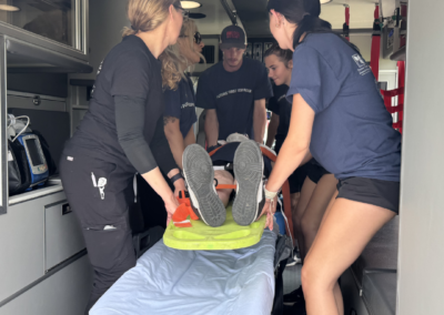 Young people in a navy shirt lift a person on a stretcher inside an ambulance