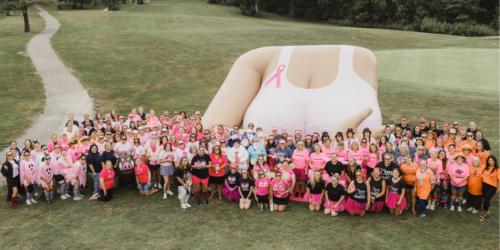 A large group of women stand on the grass in front of a large inflatable of a chest