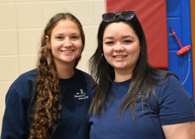 Two women in navy t-shirts stand posed next to one another