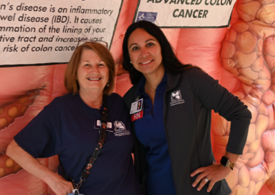 Two women stand in front of a pink inflatable displaying information about Colon Health.