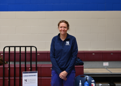 A woman in blue scrubs stands posed behind a table.