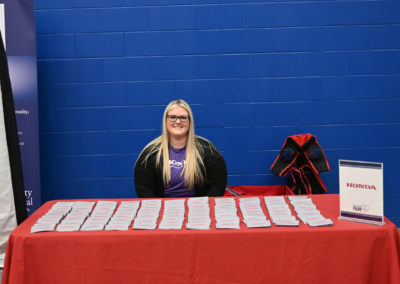 A blond woman in black sits behind a red table that says "Honda"