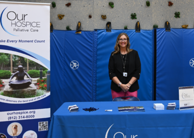 A woman in black stands behind a blue table that says "Our Hospice"