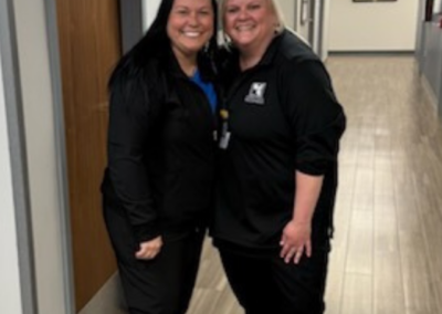 Two women dressed in black stand posed with an arm around one another