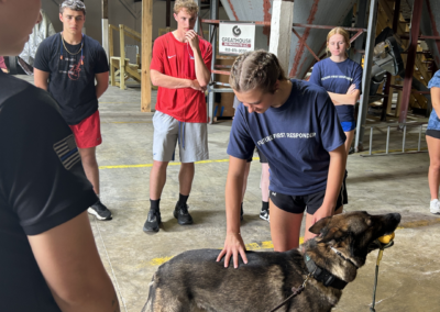 Young people stand as a person in a navy shirt pets a Police K9 German Shepard