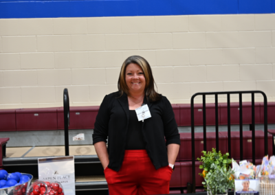 A woman in black with red pants stands behind a table with paper materials and a plant.
