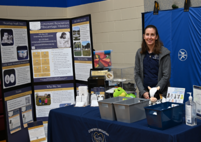Woman stands behind a table with a navy tablecloth and paper materials.