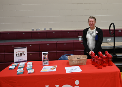 A woman in a white shirt and black sweater stands behind a red table that says "HSI, Human Services Inc."