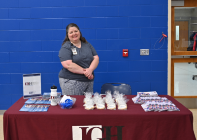 A woman in a gray shirt stands behind a maroon table with promotional materials that says "IGH, Indianapolis Gastroenterology and Hepatology"
