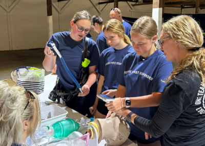 Young women in navy shirts stand over a manikin and complete the insertion of a breathing tube