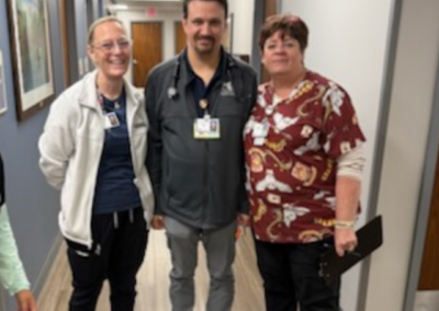 Two women stand next to a man posed together in front of a hallway