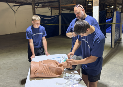 Young men stand near white table with manikin and place oxygen mask on manikin