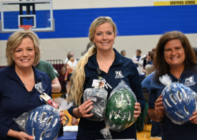 Three women in blue scrubs hold bicycle helmets