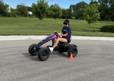 Young woman wearing goggles drives go kart outdoors with trees in the background