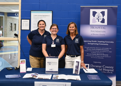 Three women in navy polos stand posed behind a table with a nice tablecloth and paper materials.