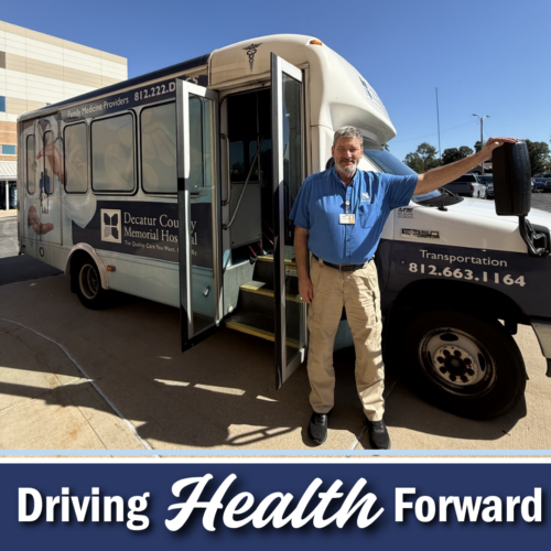 man in blue shirt and khaki pants stands posed in front of a blue and white bus ouside