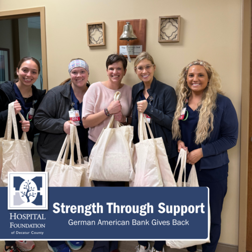 5 women stand posed together in front of a wall holding white tote bags