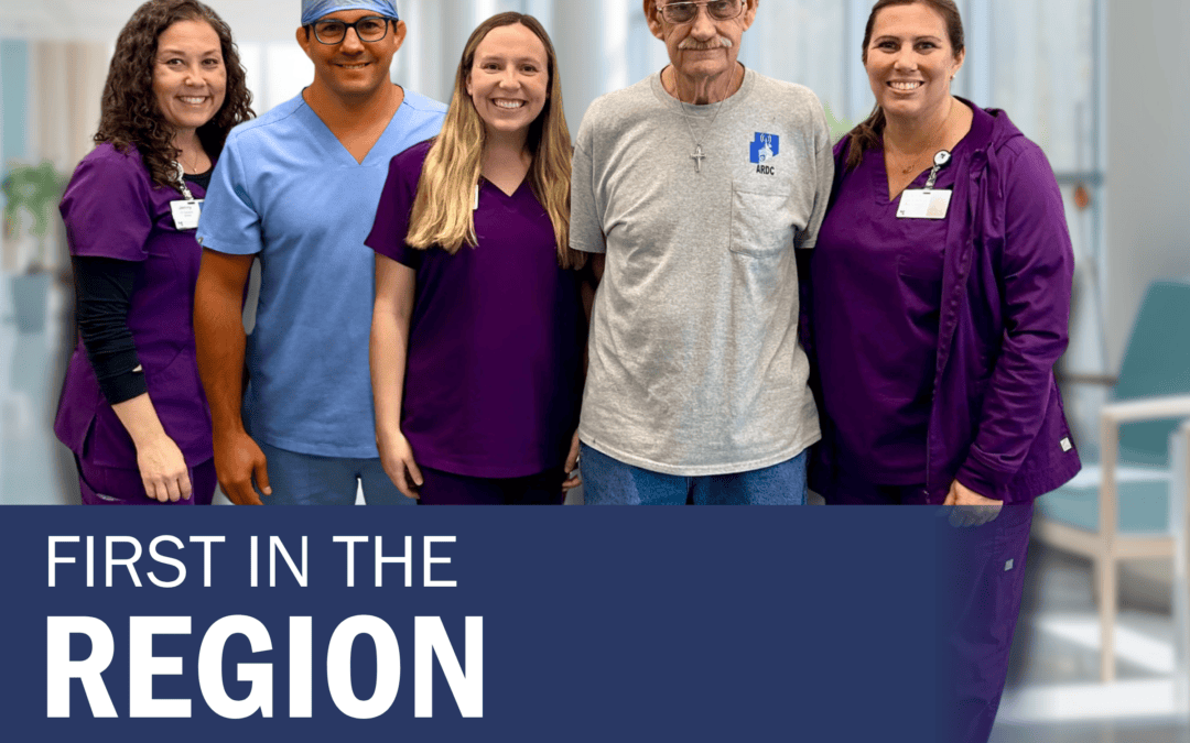 A woman with brown curly hair and purple scrubs, a man in light blue scrubs with glasses, a woman with blonde hair and purple scrubs, a man with a gray t-shirt and glasses, and a woman with brown hair pulled into a pony tail and purple scrubs stand posed together for a photo.