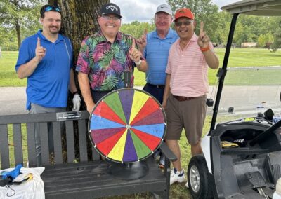 Four men in golf clothing stand in front of a tree holding up a #1